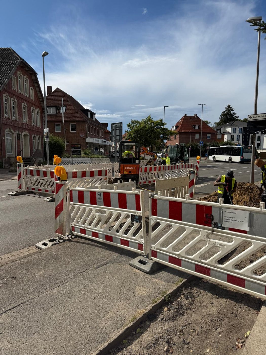 Tiefbauarbeiten an einer Straßenverzweigung mit Minibagger und Absperrung