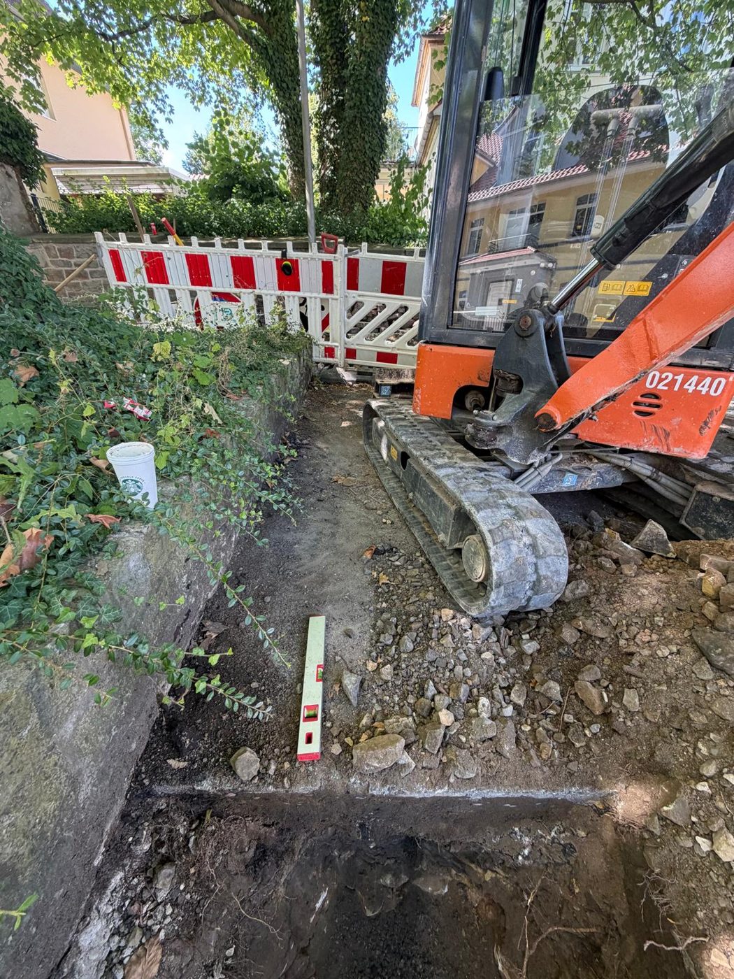 Minibagger und Wasserwaage bei Schachtarbeiten an einer Mauer